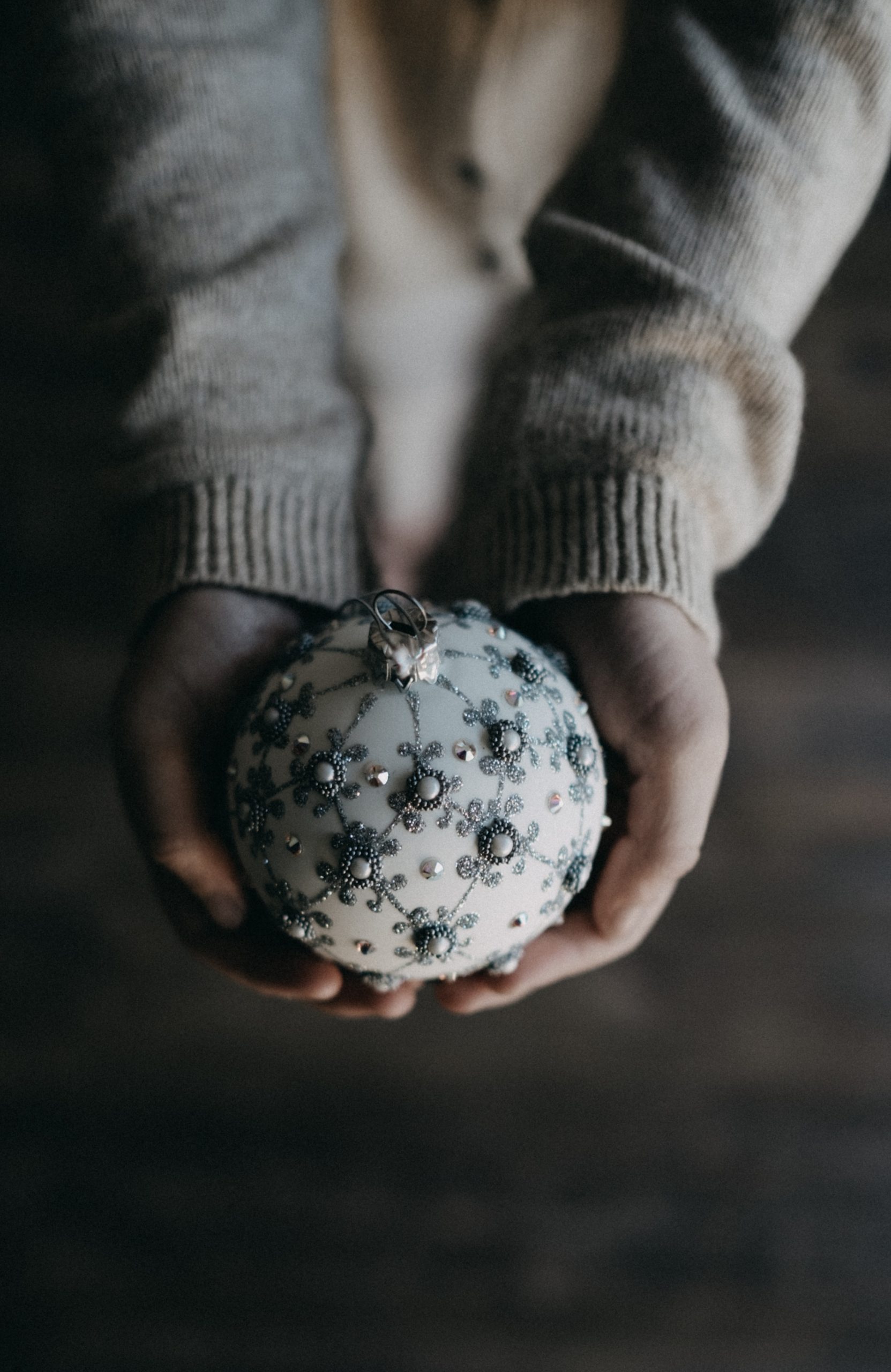 arms out with hands holding a white and silver christmas tree round ornament.