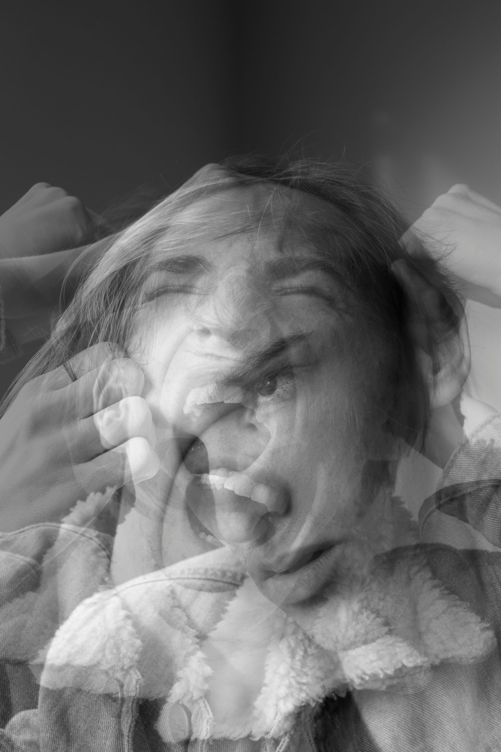 a grayscale photo of layered faces - one shaking head screaming and one staring outward