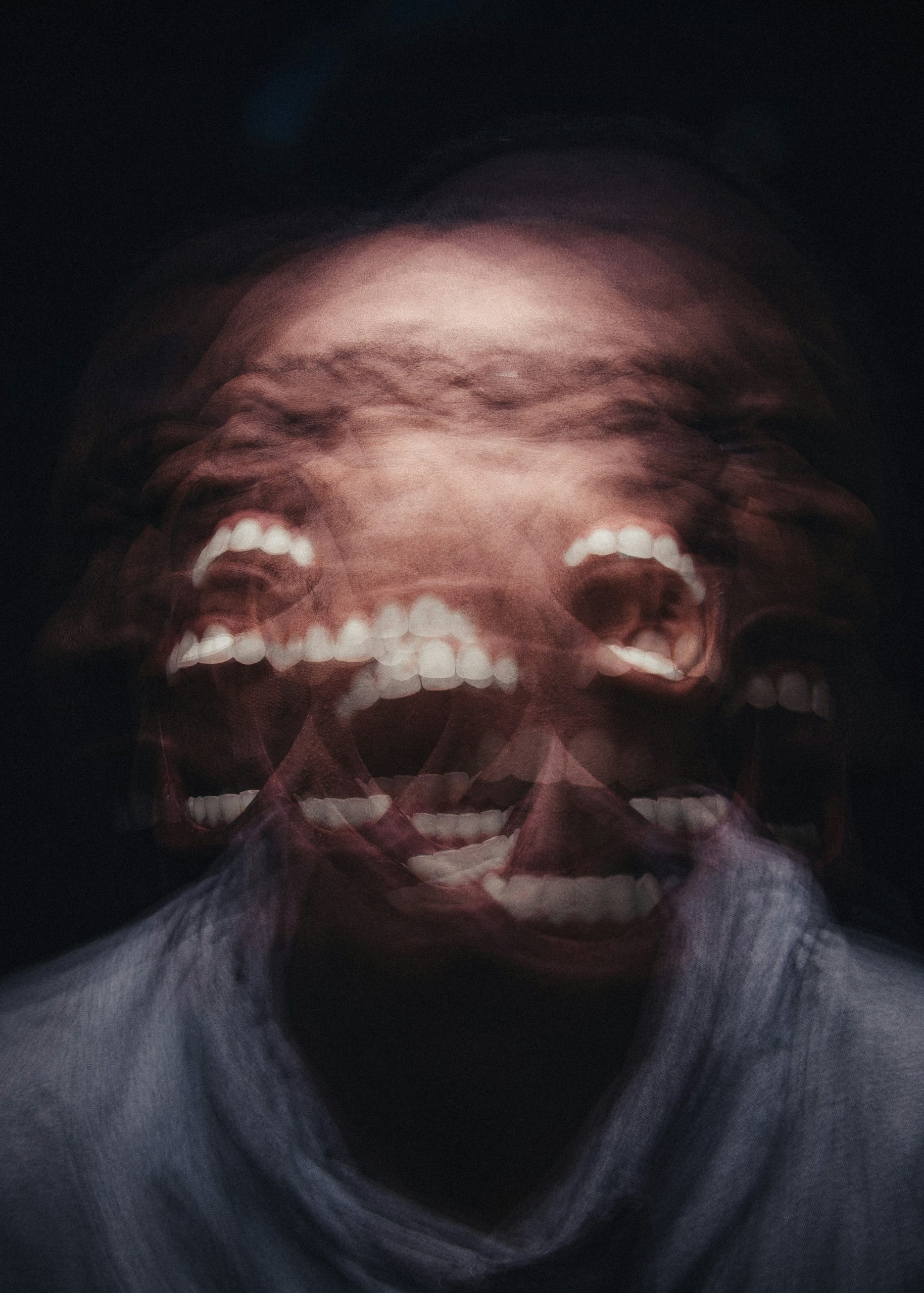 a photograph captures a face with a wide open mouth, appearing to be screaming, and shaking their face side to side. The face is blurry but you can see where the movement of the face is through the captured placement of the teeth.